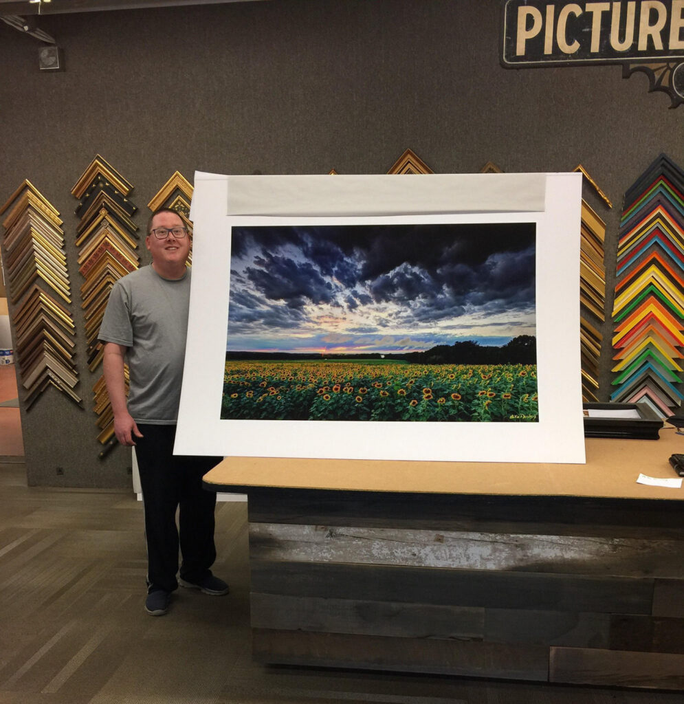 Photographer Mike Dooley holding a freshly signed print of Sunflower Under Stormy Skies, ready for framing and installation