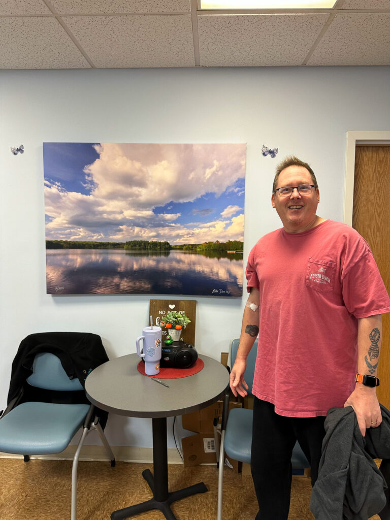 Mike Dooley holding a large fine art print at a medical lab, illustrating scale and presence of the artwork.