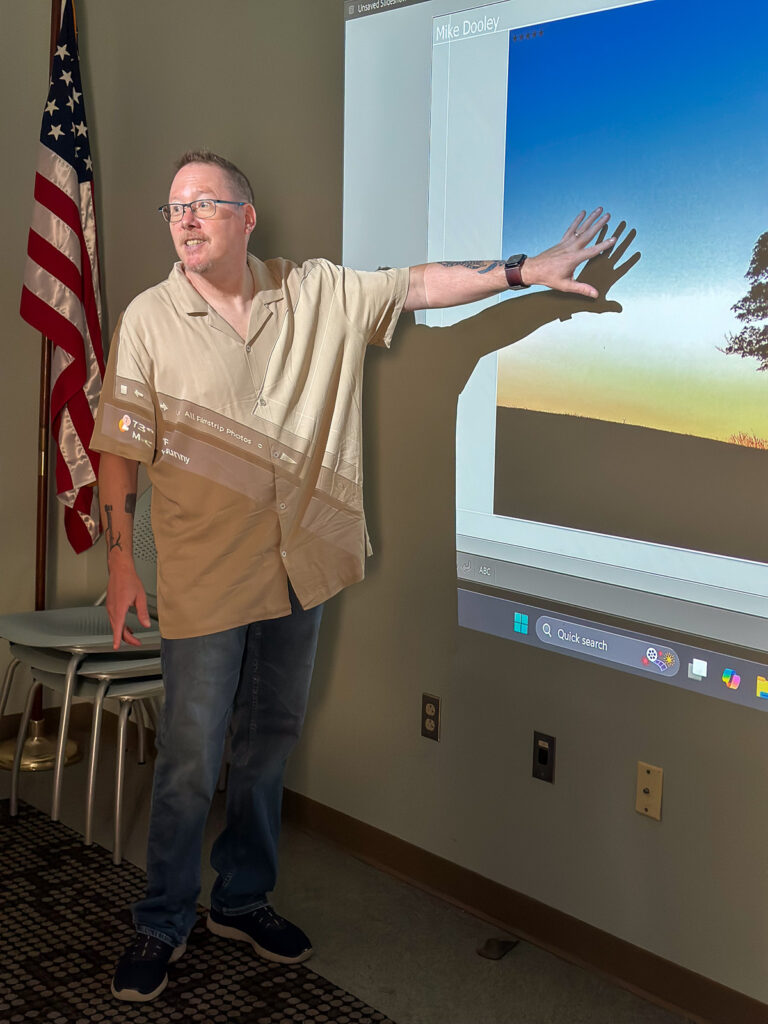 Mike Dooley teaching in a classroom setting, standing at the front and leading a photography lesson for workshop participants.