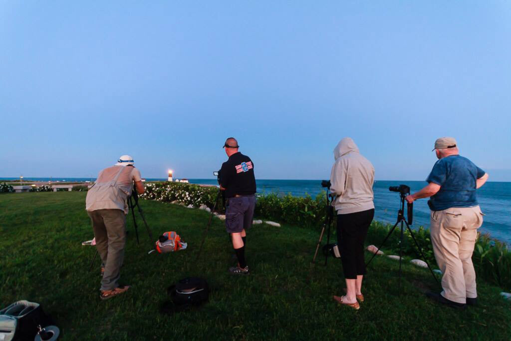 Four photography students with tripods capturing the sunset at Point Judith Lighthouse, Rhode Island, learning composition and light under Mike Dooley's guidance.