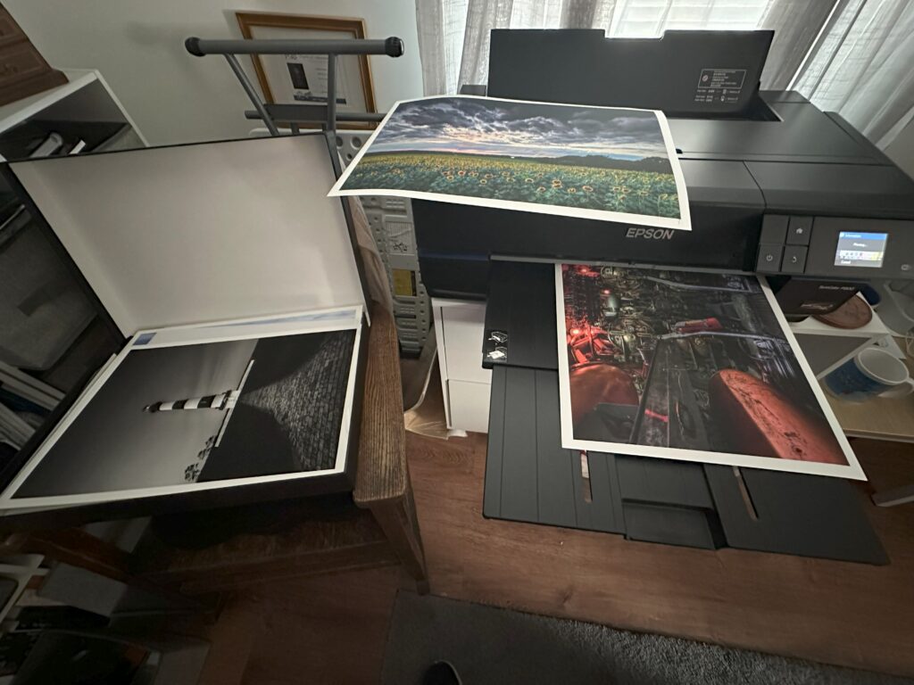 Mike Dooley’s Epson printer producing fine art photography prints, including Torpedo Room, Bodie Island Lighthouse in black and white, and Sunflowers Under Stormy Skies on Red River paper.