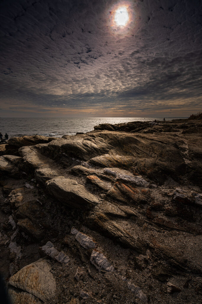Sunset over the rocky shoreline at Beavertail State Park in Jamestown, Rhode Island, with waves glowing in the golden evening light.