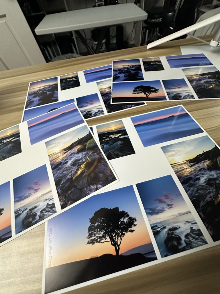 A wooden desk covered with several photo prints on different types of Red River Paper.