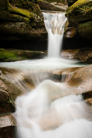 Color photograph of Sabbaday Falls in the White Mountains of New Hampshire, showing cascading water and surrounding forest, by Mike Dooley.