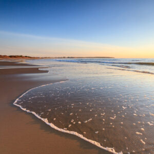 A wave rolling onto a Block Island beach at sunrise, capturing motion and morning light, photographed by Mike Dooley.