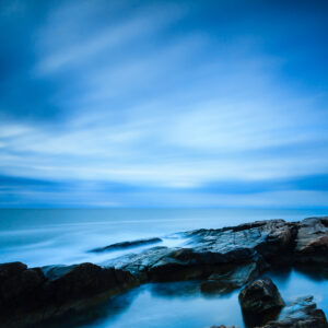 Long exposure photograph of Narragansett Beach on a cloudy blue morning, capturing smooth surf and soft light, photographed by Mike Dooley.