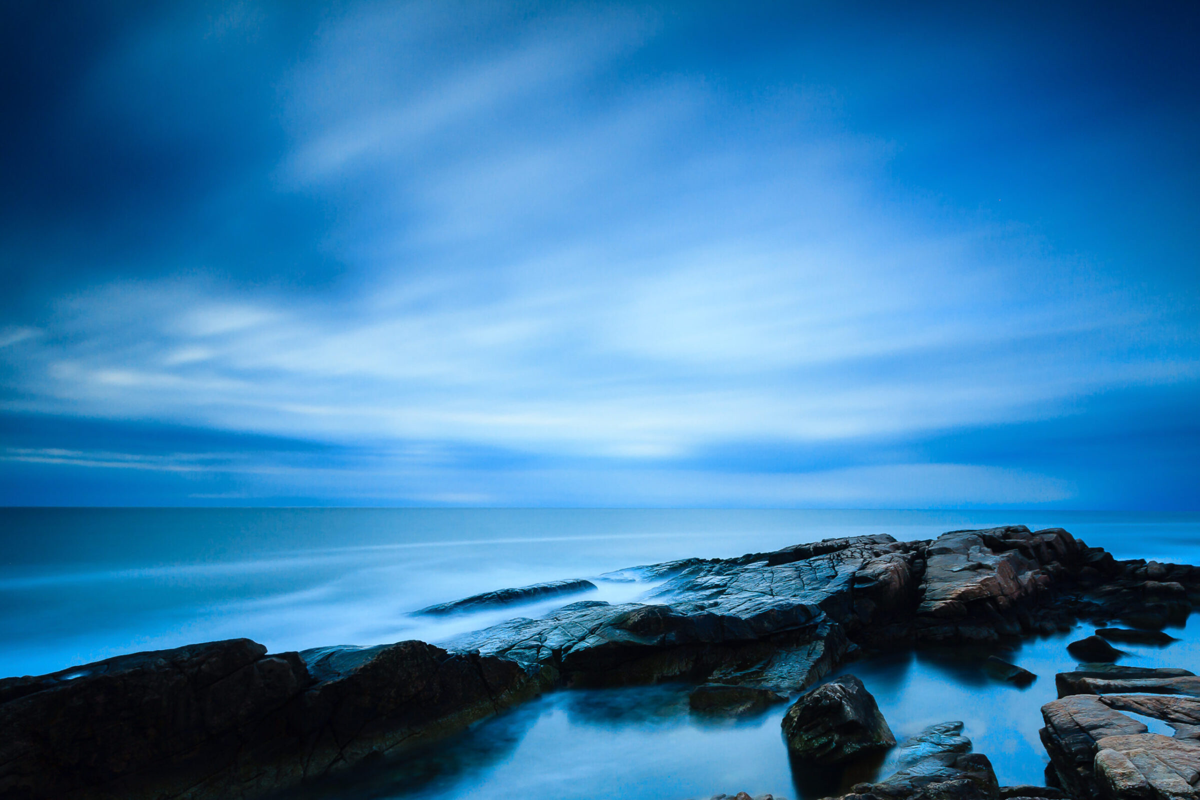 Long exposure sunrise at Newton Avenue Rocks in Narragansett Rhode Island with moving clouds and blue-toned coastal rocks