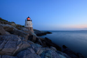 Castle Hill Lighthouse glowing red at sunset with rocky coastline in Newport, Rhode Island, photographed as a fine art print by Mike Dooley.
