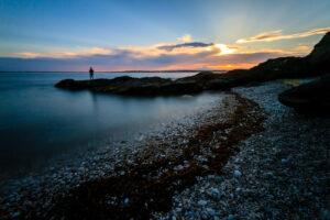 A fisherman standing on rocks at Beavertail State Park in Narragansett Bay, Rhode Island, casting a line, photographed by Mike Dooley.