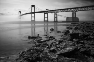 Black-and-white photograph of fog rolling over the Newport Bridge in Rhode Island, emphasizing structure and atmosphere.