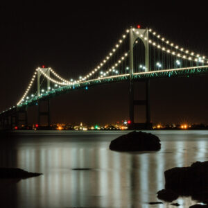 The Newport Bridge illuminated at night over calm waters, with stars in the sky, photographed by Mike Dooley.
