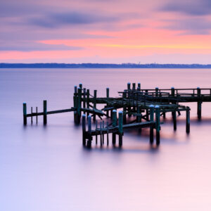 Long exposure photograph of the Rocky Point Pier ruins at sunrise, capturing smooth surf and soft light, photographed by Mike Dooley.