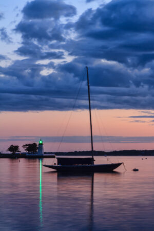 Sailboat moored in Newport Harbor with Goat Island Lighthouse in the background after sunset, photographed by Mike Dooley.