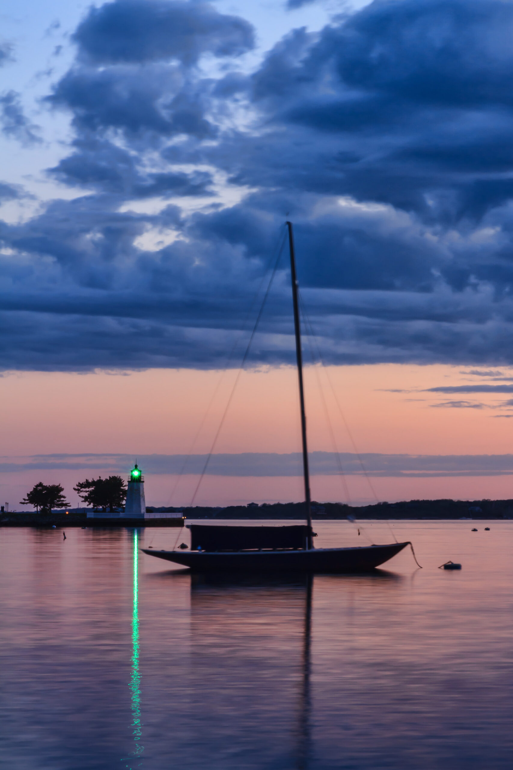 Sailboat moored in Newport Harbor with Goat Island Lighthouse in the background after sunset, photographed by Mike Dooley.