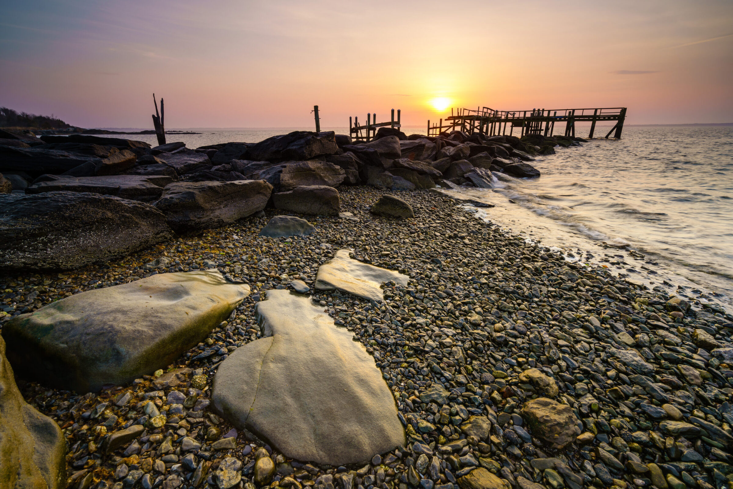 Sunrise at Rocky Point State Park, Rhode Island, with sunlight peeking behind the remains of a falling-down pier, photographed by Mike Dooley.