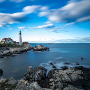 Portland Head Lighthouse at sunset in Maine, photographed by Mike Dooley Photography, with warm light illuminating the coastline.