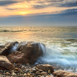 Sunset along the Massachusetts coastline at Westport, with waves crashing on a rock, photographed by Mike Dooley.