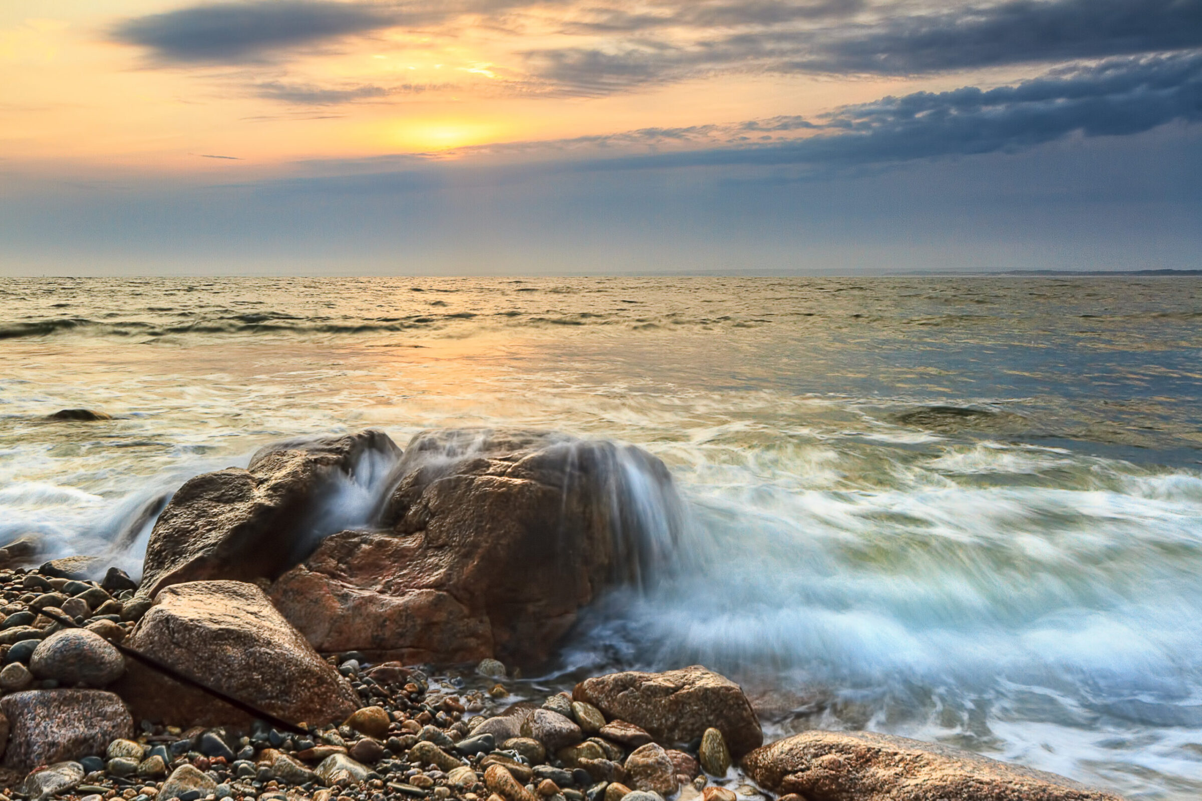 Sunset along the Massachusetts coastline at Westport, with waves crashing on a rock