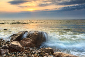 Sunset along the Massachusetts coastline at Westport, with waves crashing on a rock, photographed by Mike Dooley.