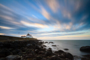 Sunrise at Watch Hill Lighthouse in Rhode Island, with streaking clouds and warm morning light, photographed by Mike Dooley.