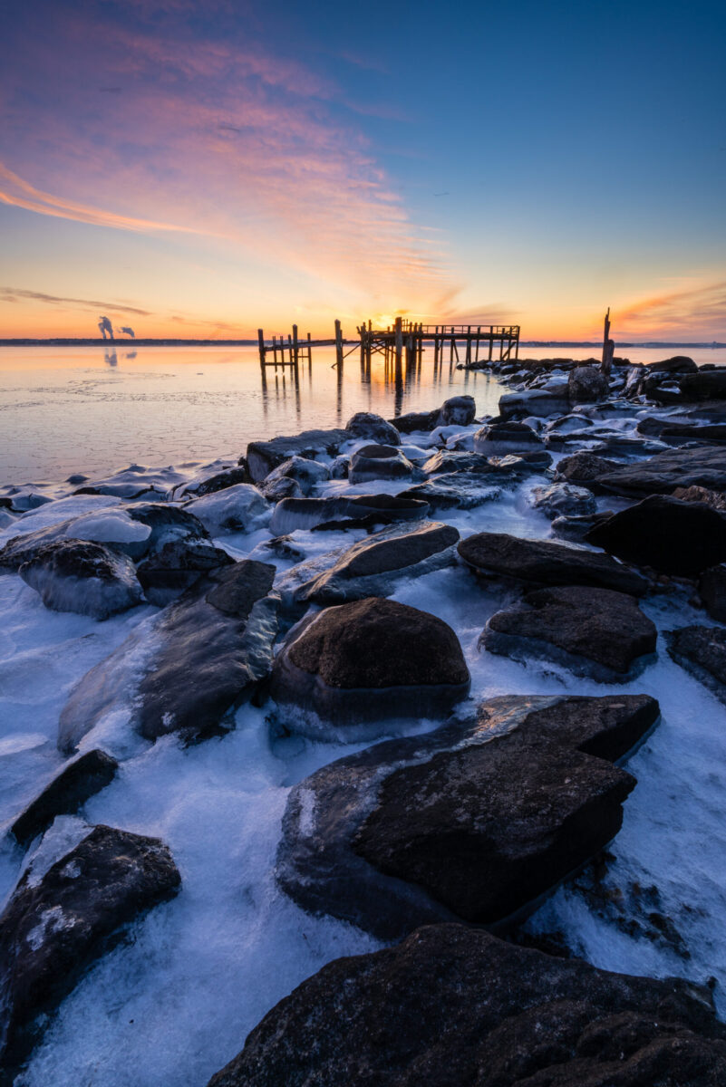 Winter sunrise at Rocky Point Park, Rhode Island, with ice-covered rocks along the shoreline