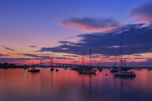 Sailboats moored in Newport Harbor at dusk under magenta clouds, Newport Bridge in the distance, Newport, Rhode Island