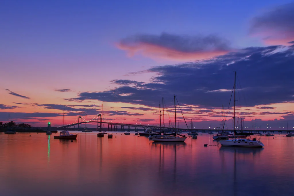 Sailboats moored in Newport Harbor at dusk under magenta clouds, Newport Bridge in the distance, Newport, Rhode Island