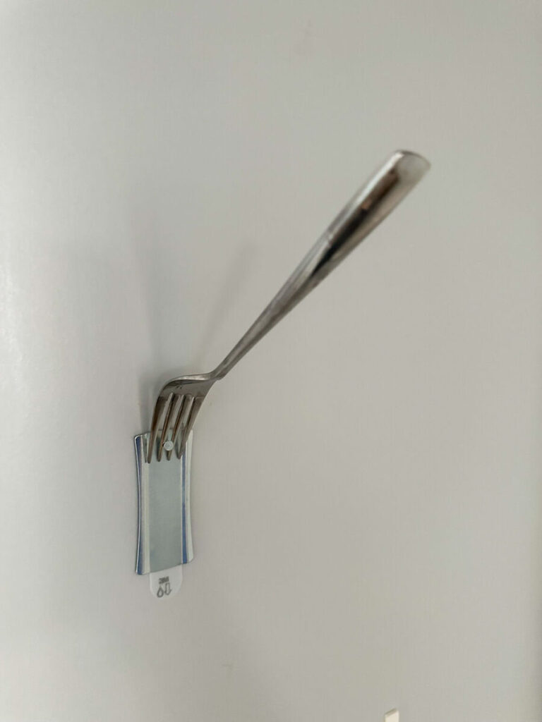 Using a fork to guide the hanging wire of a framed print onto a wall hook