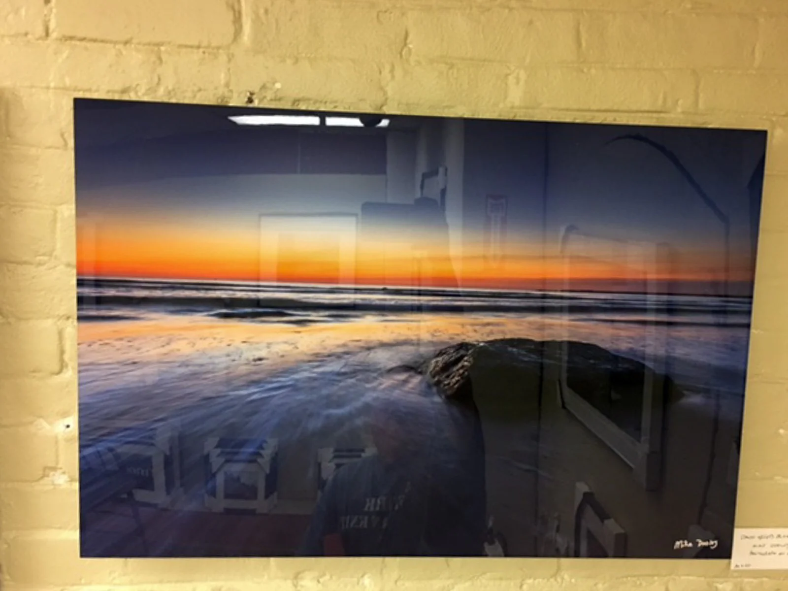 Large metal print of Dawn Greets Block Island by Mike Dooley hanging on a painted brick wall.