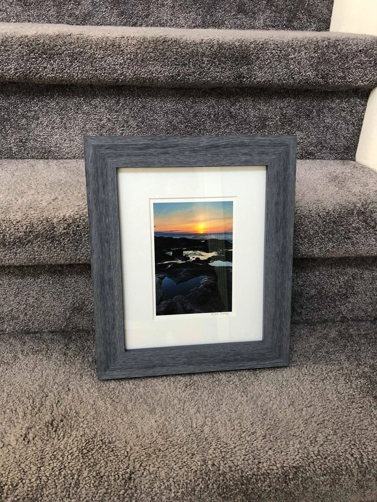 Small framed Mike Dooley sunset print leaning against a carpeted stair, ready for a client to give as a gift.