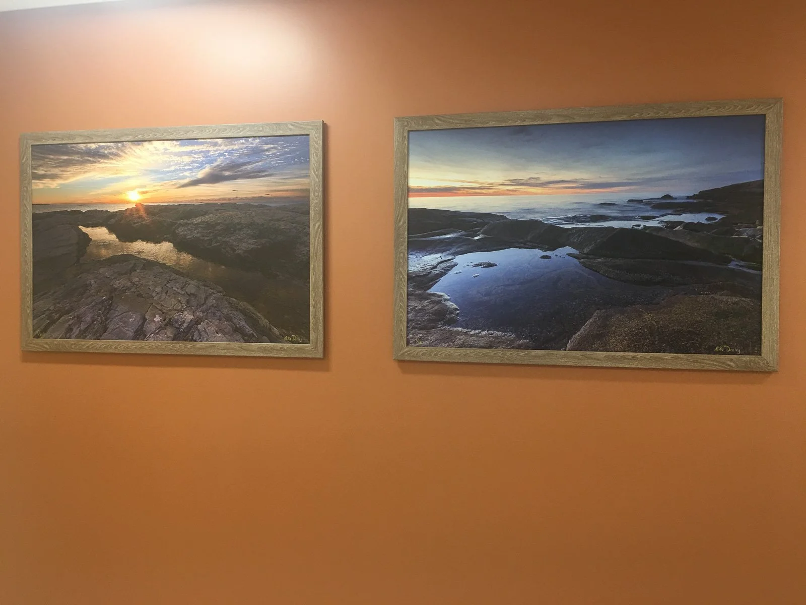 Two large framed coastal prints by Mike Dooley hanging side by side on a wall in a medical building.