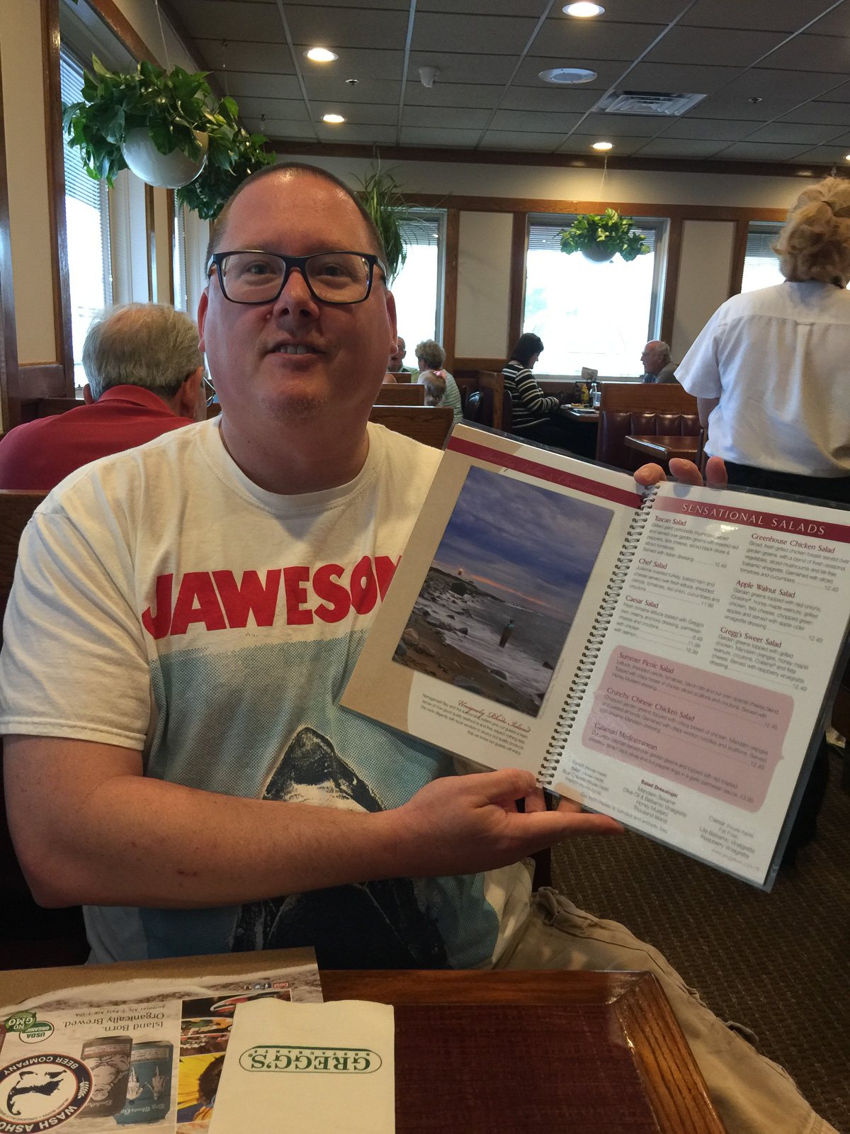 Mike Dooley holding open a Gregg's Restaurant menu that features his photographs.