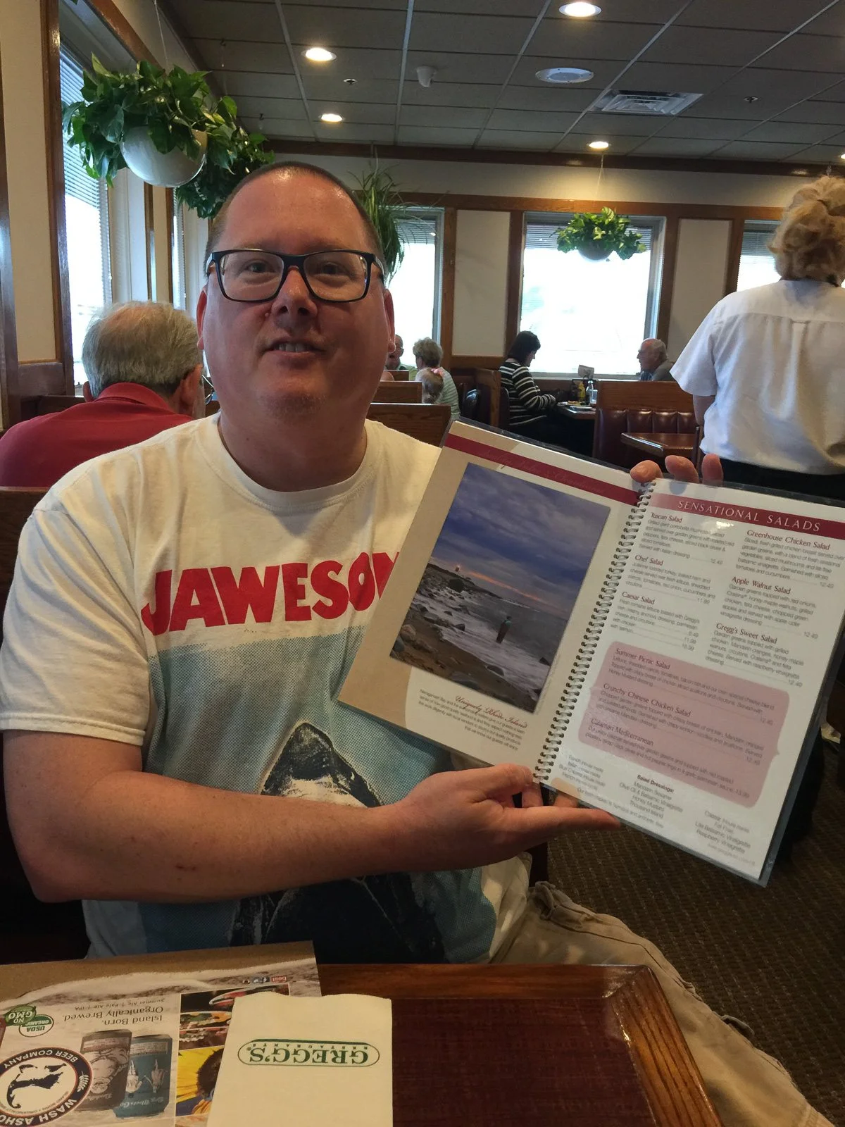 Mike Dooley holding open a Gregg's Restaurant menu that features his photographs.