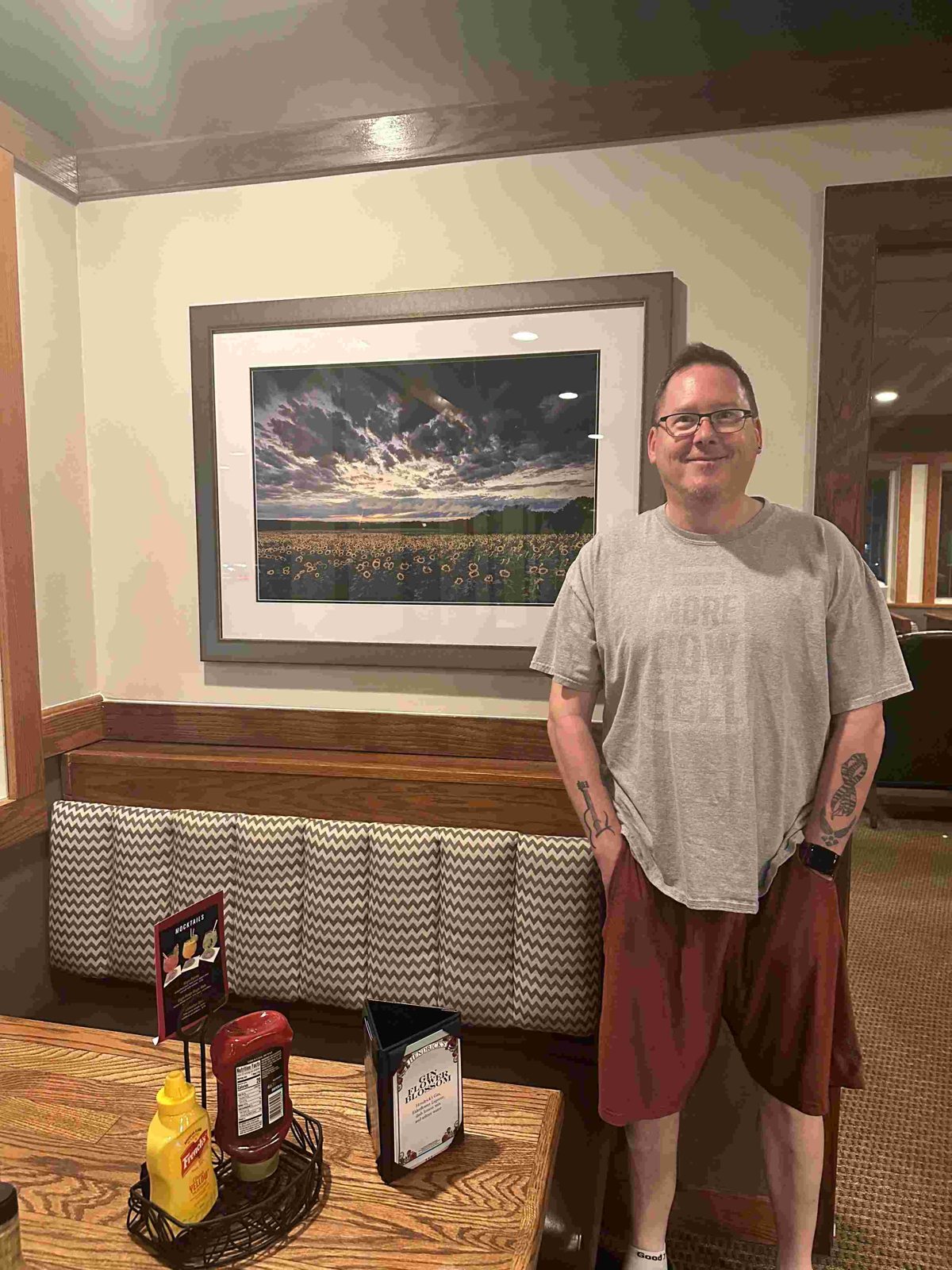 Mike Dooley standing beside his framed print Sunflowers Under Stormy Skies at Gregg's Restaurant and Tavern in Warwick, Rhode Island.