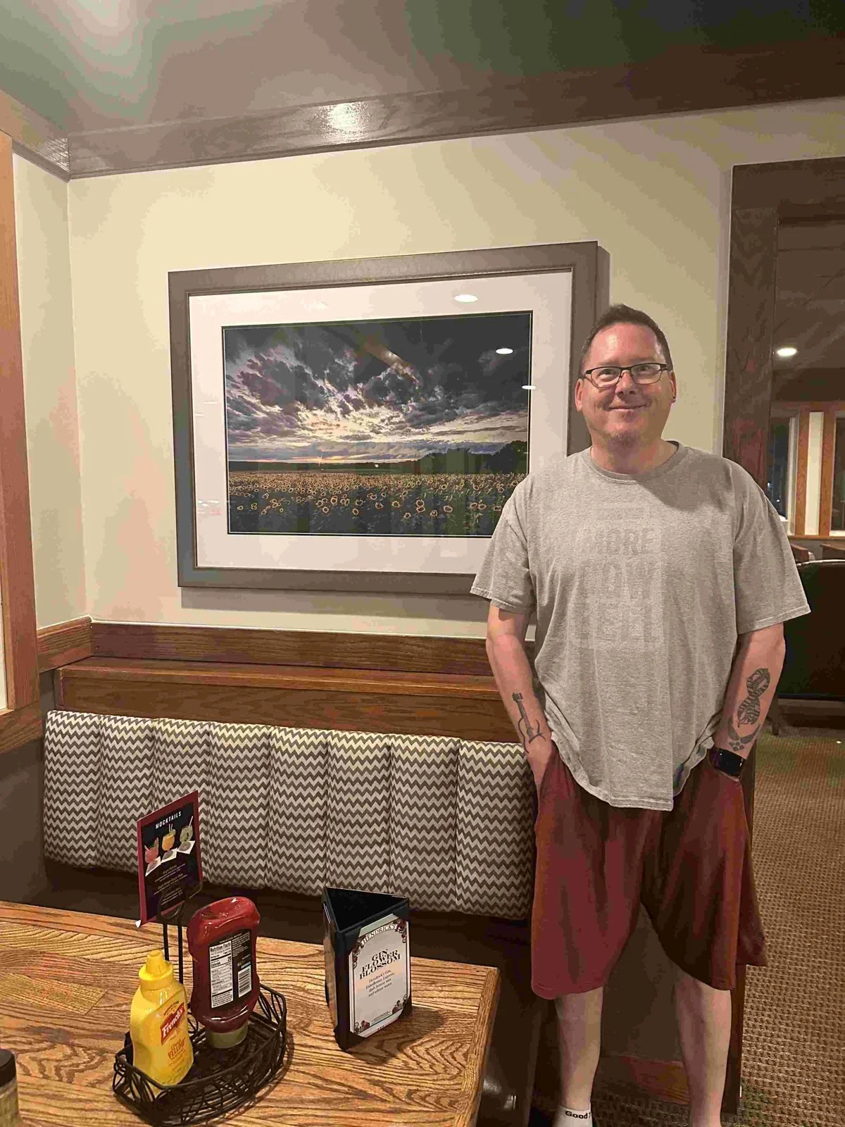 Mike Dooley standing beside his framed print Sunflowers Under Stormy Skies at Gregg's Restaurant and Tavern in Warwick, Rhode Island.
