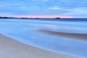 Curve of wet sand reflecting a blue sky with a pink band on the horizon at sunrise, Narragansett Beach, Rhode Island, by Mike Dooley