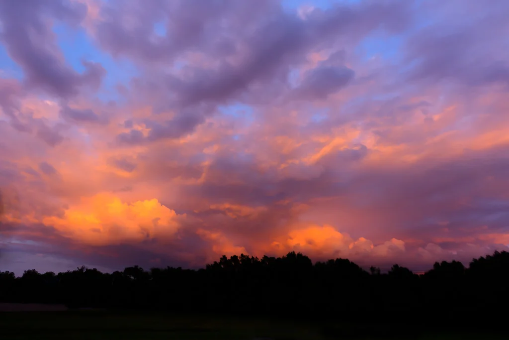 Purple and orange storm clouds at sunset over silhouetted trees, Rhode Island, fine art photograph by Mike Dooley