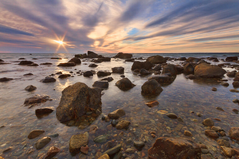 Sunset starburst over rocks in clear shallow water at Gooseberry Island, Westport, Massachusetts, photographed by Mike Dooley