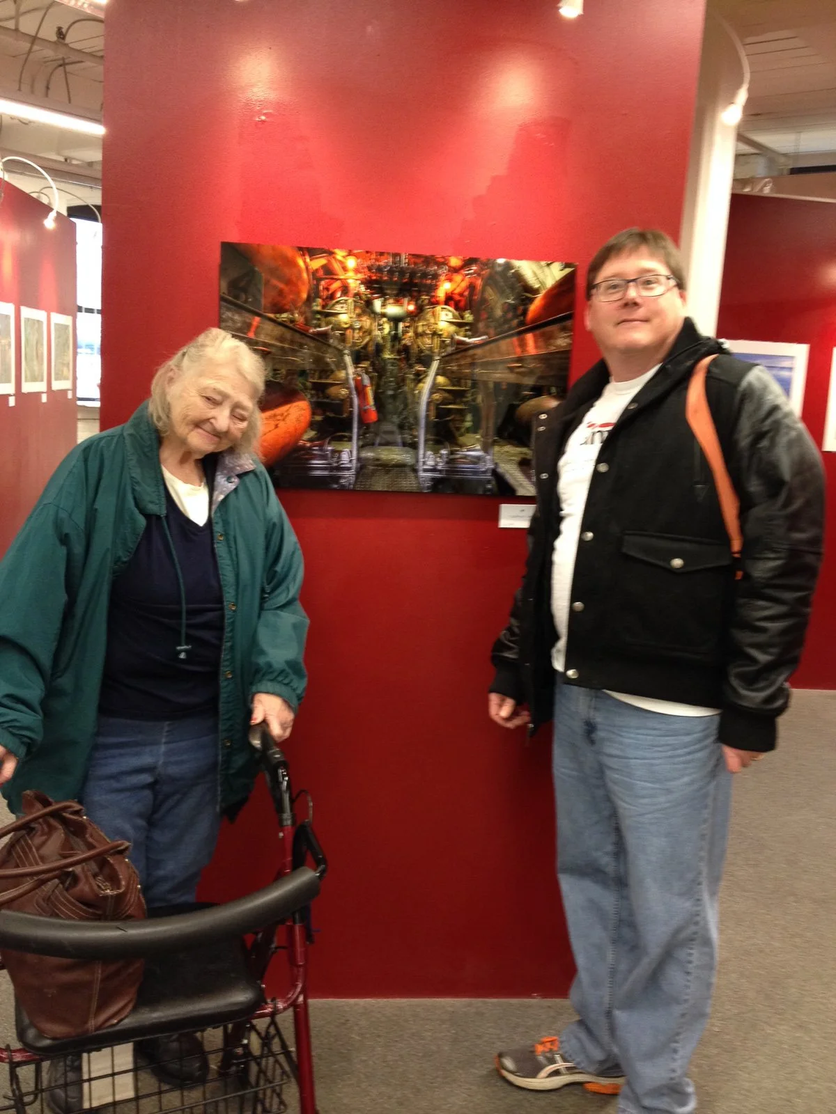 Mike Dooley and his mother-in-law standing in front of a large print of The Torpedo Room at his solo show at the Dryden Gallery in Providence.