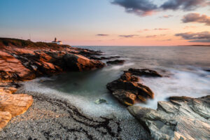 Beavertail Lighthouse on the point above warm-lit rocks and a cove at sunset, Jamestown, Rhode Island, by Mike Dooley